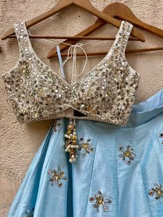 A three-piece Aqua Blue and Ivory Mirror Ruffle Lehenga Set from the Priti Sahni collection. This elegant raw silk aqua blue lehenga with mirror butti detail, sequin and ruffle border is paired with an ivory blouse in raw silk fabric with mirror, pearl and beads hand work embroidery. The lehenga has side hanging ball tassels to the waistline. This outfit is completed with an ivory tulle dupatta in net material with sequin work scalloped edging. Lehenga White, Contrast Outfit, Intricate Mirror, Ruffle Lehenga, Mirror Beads, Off White Saree, Golden Blouse, Mirror Work Lehenga, Raw Silk Lehenga