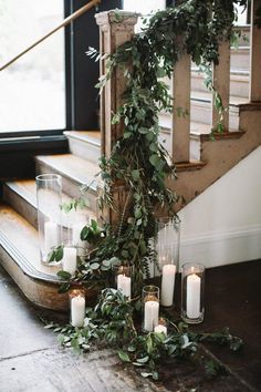 candles and greenery are arranged on the floor next to an open window with stairs in the background