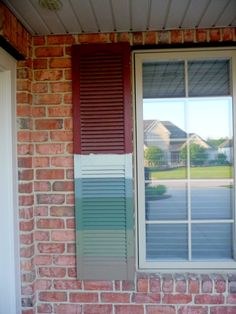 an open window on the side of a brick building with red shutters and white trim