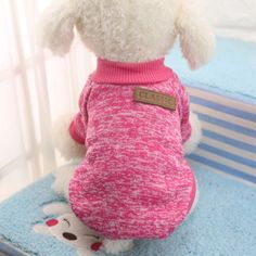 a white dog wearing a pink sweater on top of a bed