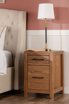 a nightstand with a lamp on it next to a bed in a room that has pink walls