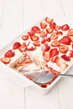 a dessert dish with strawberries and cream in it on a white wooden table next to a spoon