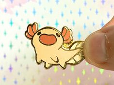 a hand holding a gold pokemon pin with red eyes