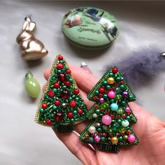 a hand holding two christmas trees made out of bead and glass beads, next to other ornaments