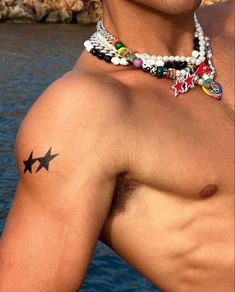 a shirtless man with tattoos on his chest next to the water and rocks in the background