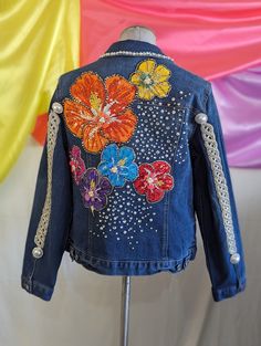 a denim jacket with colorful flowers on the back and beadings around the shoulders