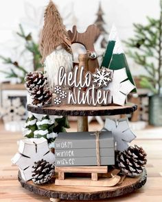 a three tiered tray with pine cones on it and the words hello winter written in white