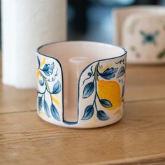 a close up of a cup on a table with two rolls of toilet paper in the background