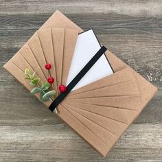 four brown envelopes with black ribbon and red berries on them, sitting on top of a wooden table