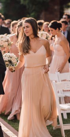 a woman in a long dress walking down the aisle at a wedding with her bridesmaids