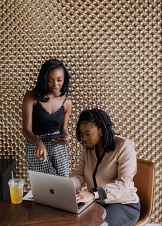 two women sitting at a table looking at a laptop