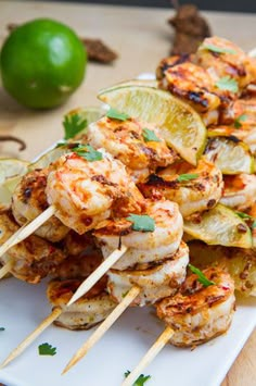 grilled shrimp skewers with lemon wedges and cilantro on a white plate