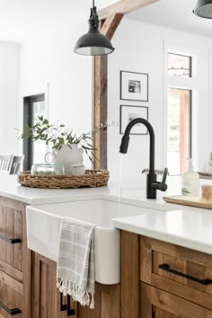 a kitchen with wooden cabinets, white counter tops and black pendant lights over the sink