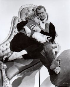 a man and woman sitting on a couch with their arms around each other, embracing