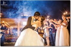 a bride and groom kissing in front of their wedding party with sparklers at night