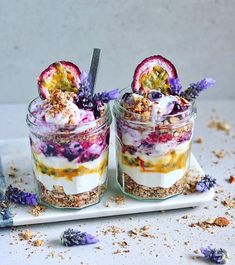 two desserts with fruit and granola in glass jars on a white platter