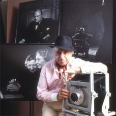 a man in a hat is taking a photo with an old fashioned camera and some pictures on the wall behind him