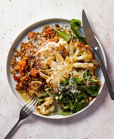 a white plate topped with cauliflower and greens next to a fork on top of a table