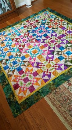 a multicolored quilt is laying on the floor next to a mirror and rug