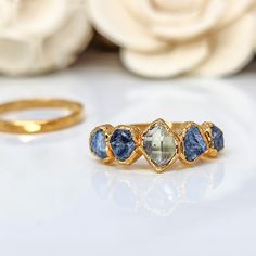 three stone ring sitting on top of a white table next to flowers and a gold band