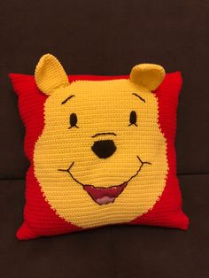 a crocheted winnie the pooh pillow is sitting on a brown couch with a black background