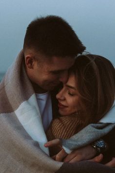 a man and woman wrapped in a blanket by the ocean