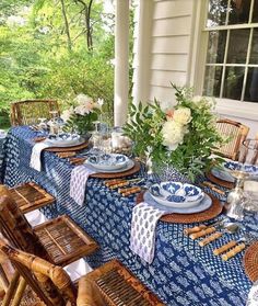 an outdoor table set with blue and white plates, napkins and place settings on it