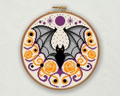 a cross - stitch pattern with a bat and flowers on it's hoop hanging from the wall