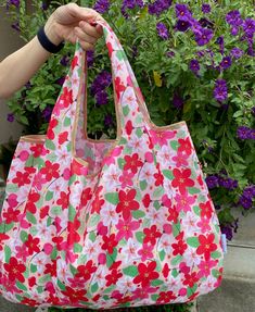 a person holding a pink flowered bag in front of purple flowers