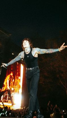 a man with tattoos on his arm and arms outstretched in front of an audience at a concert