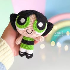 a hand holding a small crocheted doll in front of a colorful background with lights