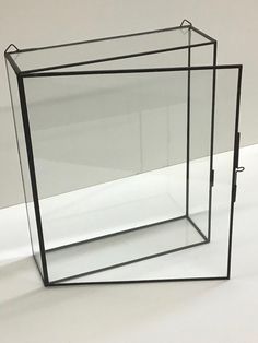 an empty glass box sitting on top of a white table next to a black metal frame