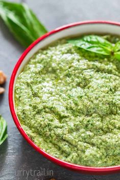 a red bowl filled with green pesto next to nuts and leaves on a table