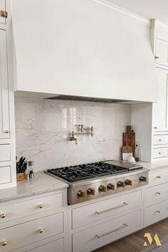 a white kitchen with marble counter tops and gold knobs on the oven hood is shown