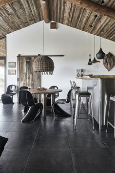 an open kitchen and dining area with black tile flooring, exposed wood ceiling and white walls