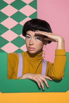 a woman with short black hair is posing in front of a green and pink wall