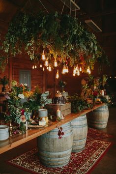 a wooden table topped with lots of barrels filled with flowers and greenery on top of a rug