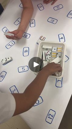 two children are playing with dominos on a white tablecloth that has blue letters and numbers