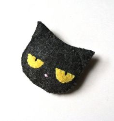 a black cat brooch with yellow eyes on it's head and ears, sitting on a white surface