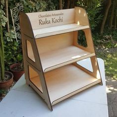 a wooden book shelf sitting on top of a table in front of some bushes and trees