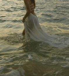 a woman standing in the water wearing a white dress