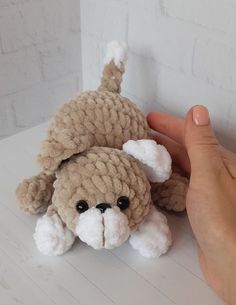 a hand holding a small stuffed animal on top of a white table next to a brick wall