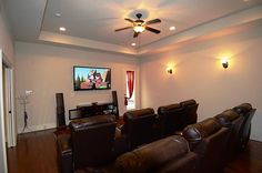 an empty theater room with brown leather chairs and a flat screen tv on the wall