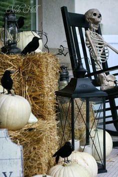 a porch decorated for halloween with pumpkins, hay and black birds sitting on chairs