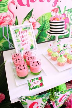 a table topped with cupcakes and desserts next to a pink flamingo wall