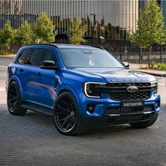 a blue truck parked in front of a tall building on a brick road next to trees