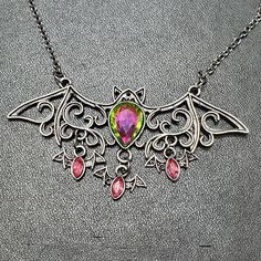 Gorgeous Silver Colored Necklace Has One Bat In Flight With A Blue/Green/Yellow/Pink Rhinestone. Hanging From The Large Bat Are Three Smaller Bats With Pink Rhinestones. Gothic Sterling Silver Necklaces For Parties, Pink Jeweled Metal Necklace, Pink Metal Necklace With Jewels, Gothic Purple Necklace For Party, Pink Nickel-free Metal Necklace, Bat In Flight, Nickel-free Pink Metal Necklaces, Ornate Purple Gemstone Necklaces, Bat Necklace Aesthetic