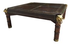 an antique leather coffee table with brass decorations on the top and legs, sitting against a white background