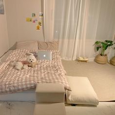 a small white dog laying on top of a bed next to a laptop and ottoman