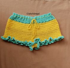 a crocheted yellow and blue shorts with ruffles on the bottom is laying on a bed